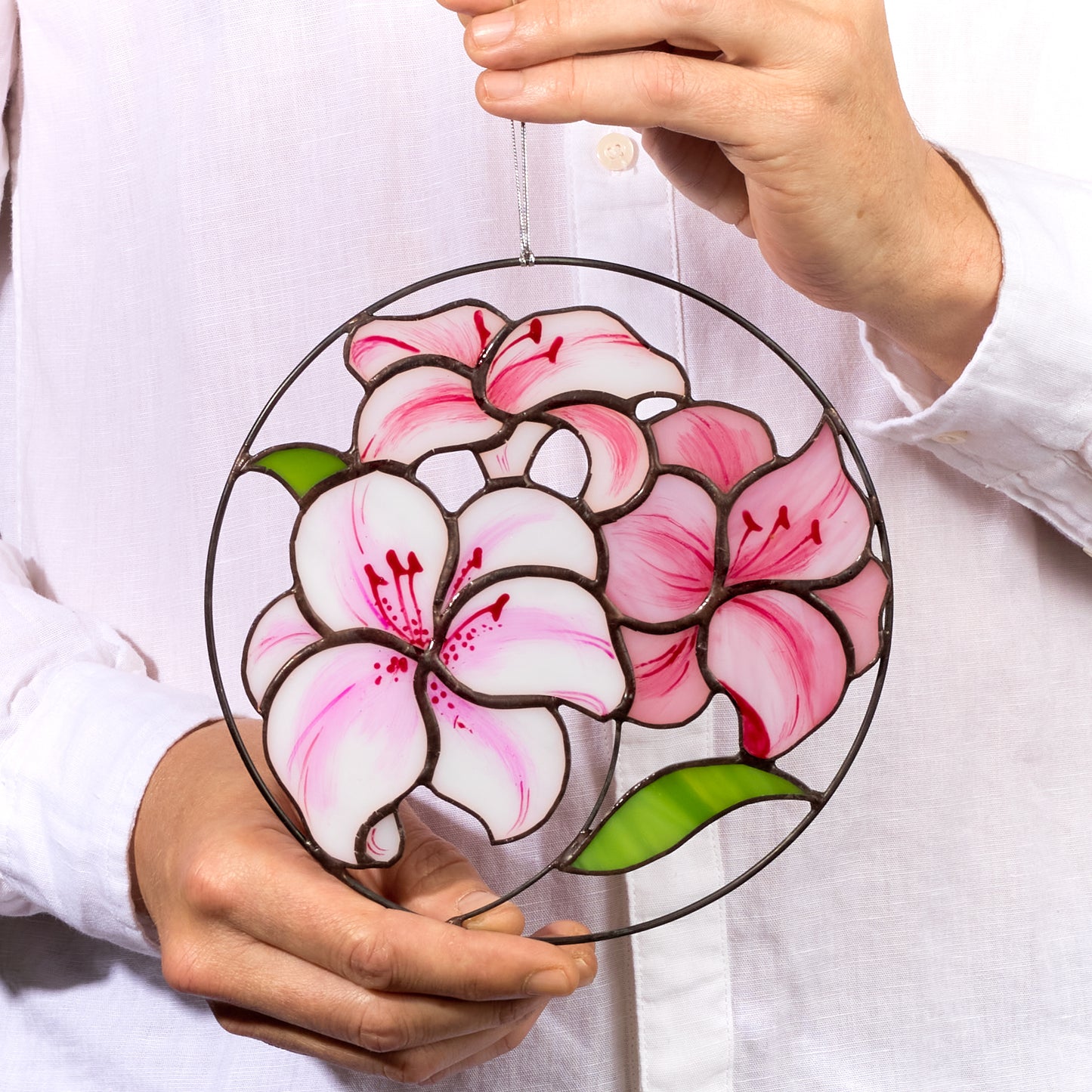 A round stained glass suncatcher featuring a floral design with pink and purple hues, held in a person's hand.