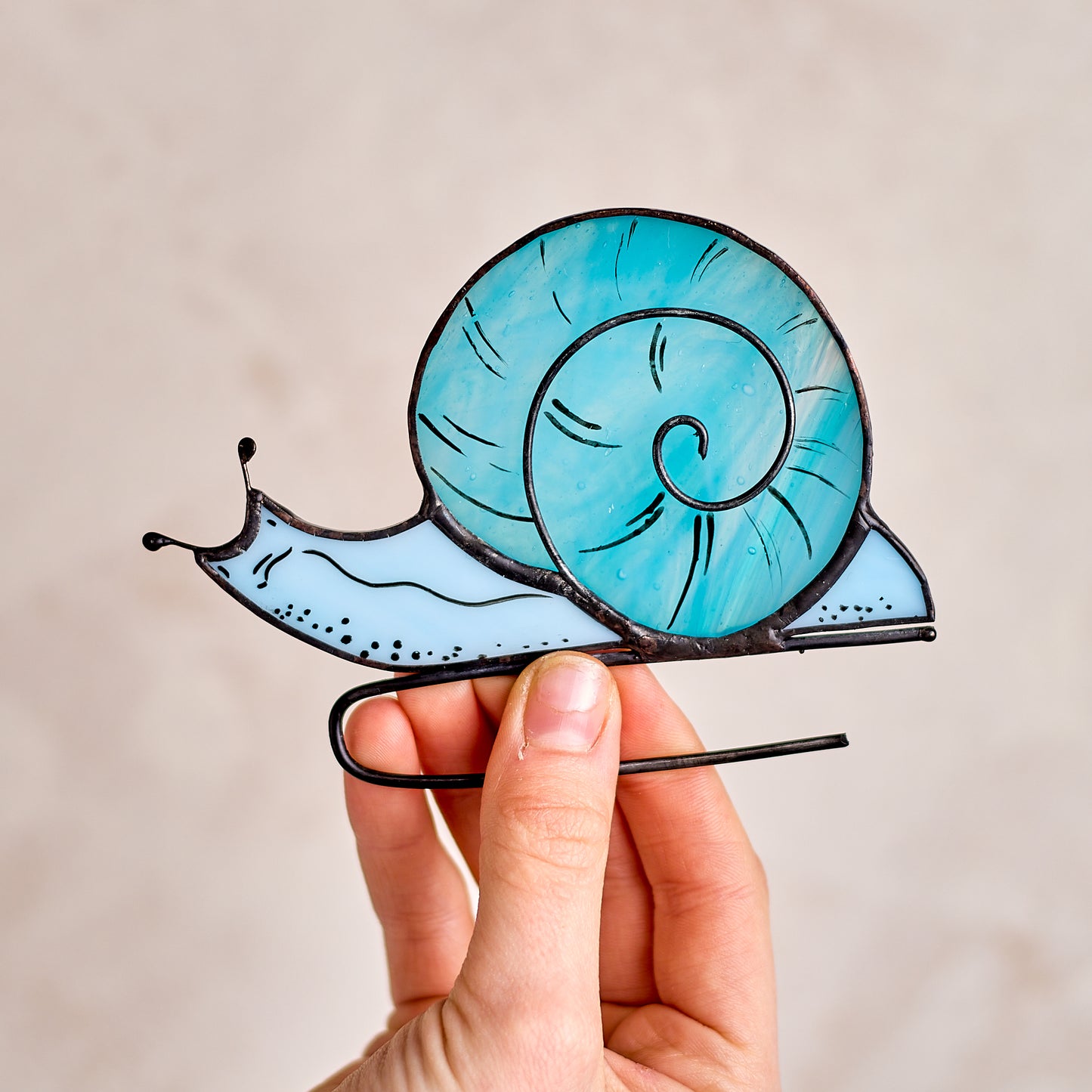 Hand holding a stained glass snail ornament against a plain background