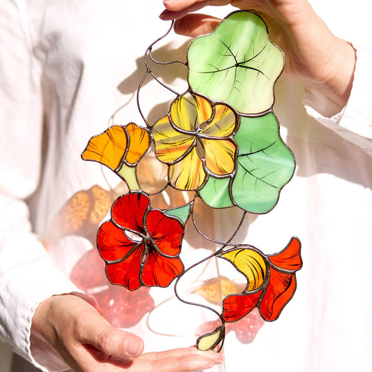 A hand holding a Nasturtium Flower Stained Glass Suncatcher with vibrant red, yellow, and green colors.
