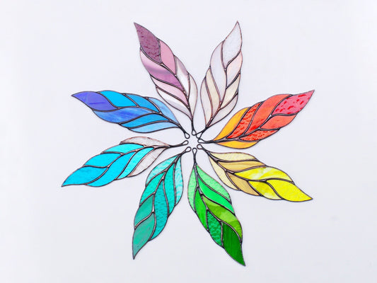 A handcrafted stained glass suncatcher in the shape of a feather with multiple colors including blue, green, yellow, and red.