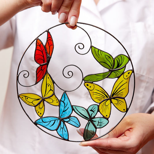 A person holding a round stained glass suncatcher with a design of flying butterflies in multiple colors.