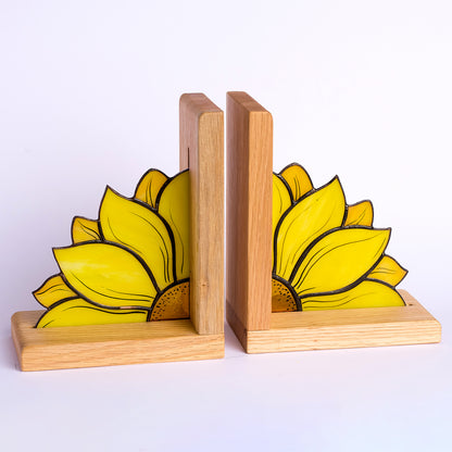A stained glass bookend in the shape of a sunflower placed on a wooden surface, holding a row of books.