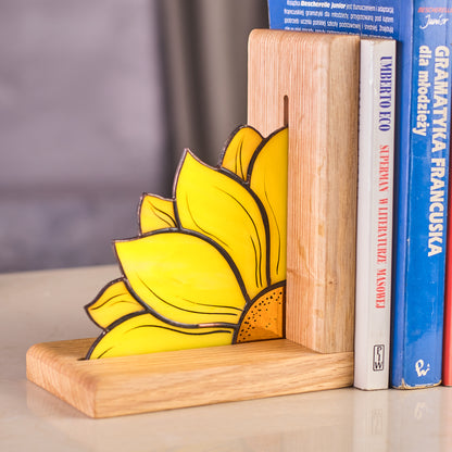 A stained glass bookend in the shape of a sunflower placed on a wooden surface, holding a row of books.