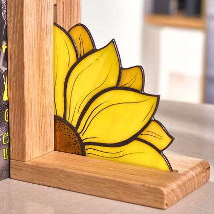 A stained glass bookend in the shape of a sunflower placed on a wooden surface, holding a row of books.