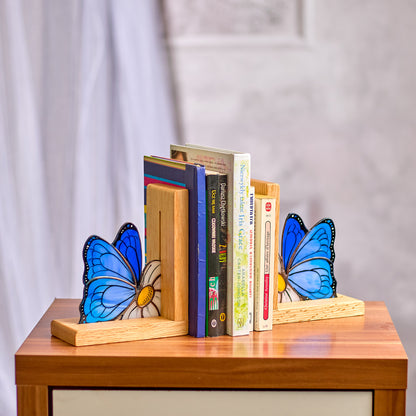 A pair of blue butterflies stained glass bookends placed on a wooden shelf, holding books on either side.