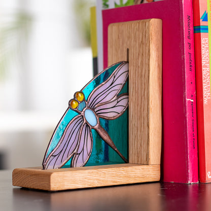 A pair of stained glass bookends with dragonfly designs, placed on a wooden base, with books stacked on top of them.