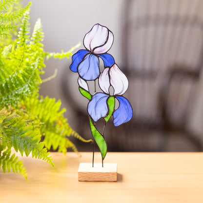 Stained glass artwork of an iris flower on a wooden stand, displayed on a tabletop.