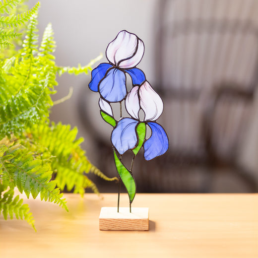 Stained glass artwork of an iris flower on a wooden stand, displayed on a tabletop.