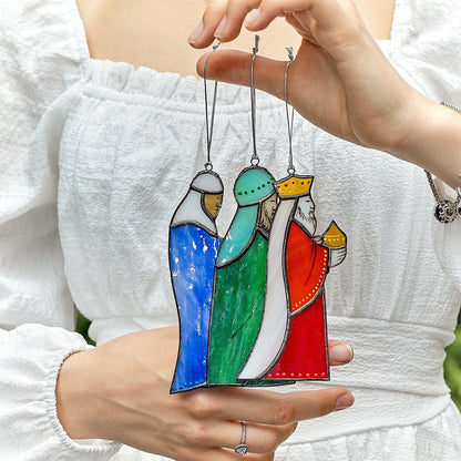 A hand holding a stained glass ornament depicting three wise men in vibrant colors with gold accents, soldered with the Tiffany technique.