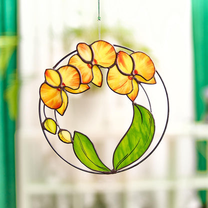A round stained glass panel suncatcher featuring yellow orchid flowers with green leaves, hanging by a window.