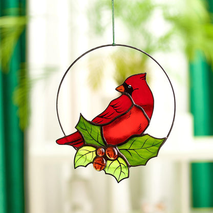 A circular stained glass suncatcher featuring a red cardinal bird with green leaves and red glass berries, hanging by a window.