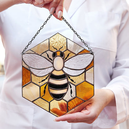 A person holding a stained glass suncatcher with a bee design and yellow and black colors.
