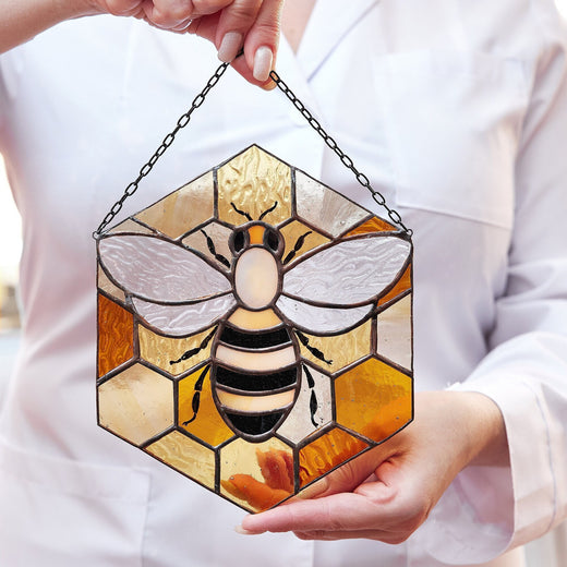 A person holding a stained glass suncatcher with a bee design and yellow and black colors.
