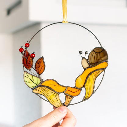 A handcrafted stained glass suncatcher featuring chanterelle mushrooms with a snail and leaves, designed for window hanging.