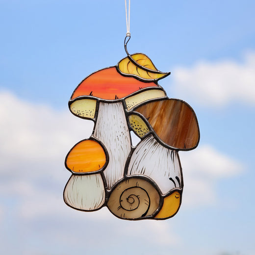 A handcrafted stained glass panel featuring a boletus mushroom with a copper foil and tin soldering, painted details, and a suction cup for hanging.