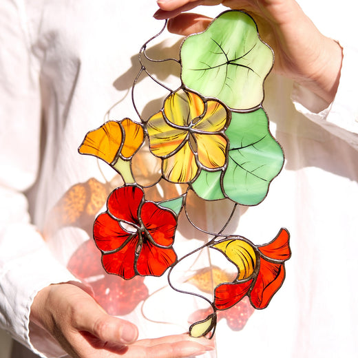 A hand holding a Nasturtium Flower Stained Glass Suncatcher with vibrant red, yellow, and green colors.