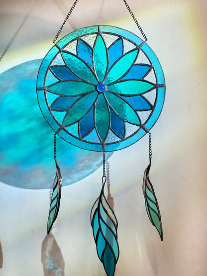 A handcrafted stained glass dreamcatcher with a blue circular pattern and feathers, intended for window hanging.