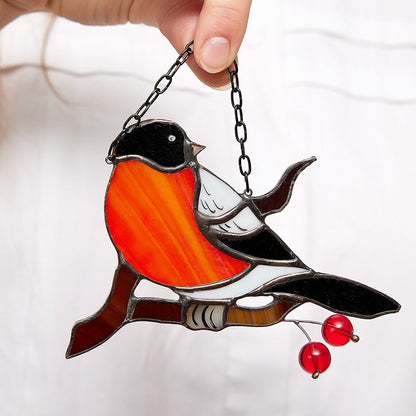A hand holding a stained glass suncatcher in the shape of a bullfinch bird with colorful art glass soldered using cooper foil and tin details.