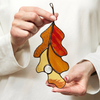 A person holding a handmade stained glass oak leaf suncatcher with autumn colors.