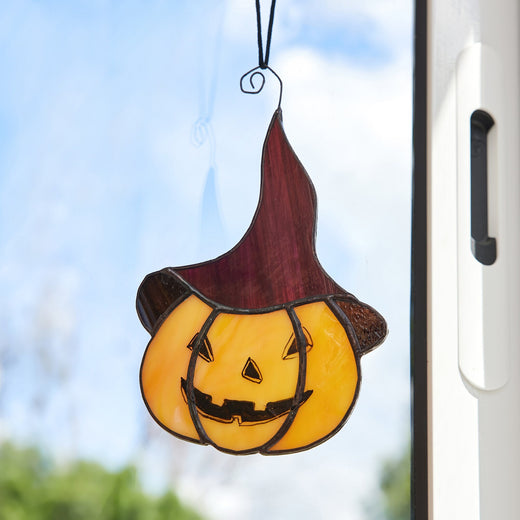 Stained glass decoration depicting a pumpkin with a mischievous face wearing a hat, designed for Halloween decoration.