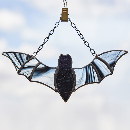 Stained glass decoration shaped like a bat with black and gray colors, hanging against a blue sky background.