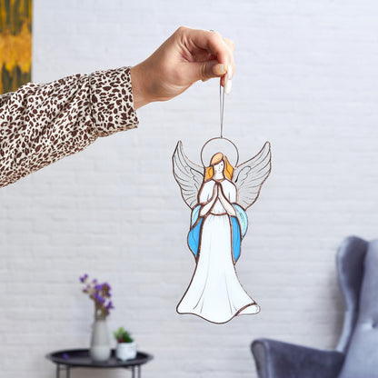 Hand holding a stained glass angel figurine with blue and white colors against a sunlit background