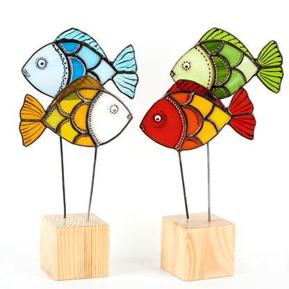 Two colorful stained glass fish figurines on top of wooden platforms, with one fish predominantly blue and the other mainly red, both featuring geometric patterns in their designs.