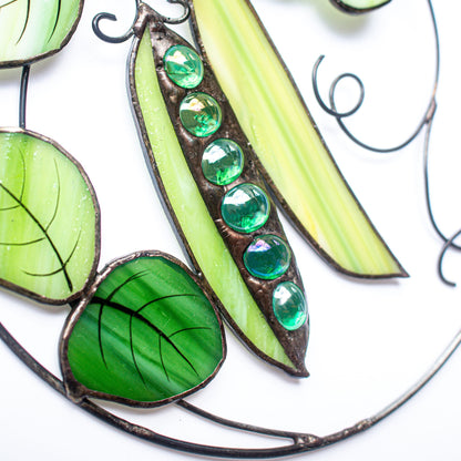 A stained glass window hanging featuring a pod of green peas with glass pieces in shades of green and a leaf on the side.